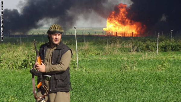 مقاتل كردي تظهر خلفه سحابة من الدخان تنبعث من حقل خباز غرب كركوك بعد استعادة البيشمرغة السيطرة عليه من تنظيم داعش، 2 فبراير/ شباط 2015 