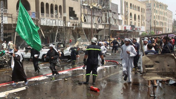 An Iraqi pilgrim holding a green flag walks past destroyed cars at the scene of a car bomb blast which targeted Shiite pilgrims on an annual march to a Baghdad shrine on May 9, 2014, killing at least seven people and wounded 20, according to security and medical sources. An Iraqi interior ministry official confirmed the attack near Kahramana square which sent a plume of dark smoke billowing into the sky above the Iraqi capital's central neighbourhood of Karrada.   AFP/PHOTO/AHMAD AL-RUBAYE        (Photo credit should read AHMAD AL-RUBAYE/AFP/Getty Images)