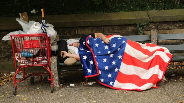 A homeless man sleeps under an American flag blanket on a park bench in New York City. New U.S. data reports a drop in the number of homeless people -- but not in New York and other states.