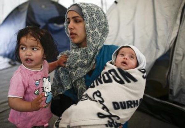 لاجئة سورية تحمل طفليها في مخيم مؤقت للاجئين والمهاجرين في قرية إيدوميني اليونانية على الحدود مع مقدونيا يوم 20 مايو ايار 2016. تصوير: كوستاس تسيرونيس - رويترز 